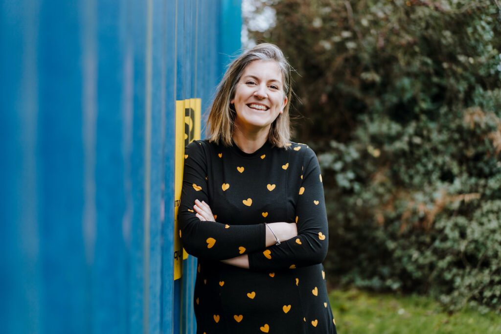 Emily from Yellow Tuxedo leaning against a blue container. Today she gives her top tips for Google My Business listings