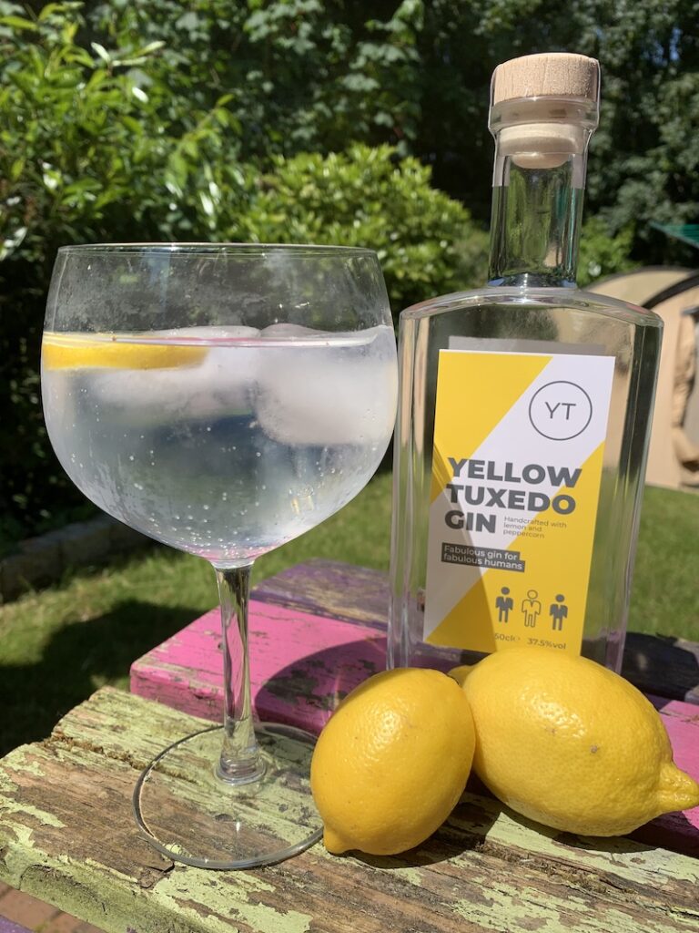 a large glass of gin and tonic beside a bottle of Yellow Tuxedo gin and two lemons.
